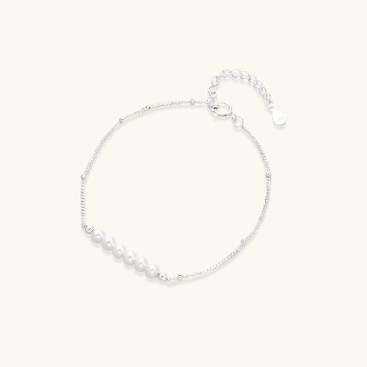 Delicate rhodium-plated silver chain bracelet with row of small baroque pearls centered on white background.