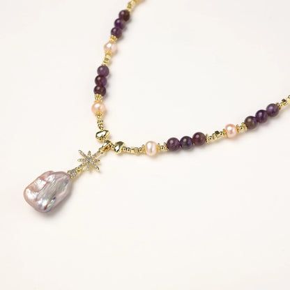 Gold necklace with iridescent baroque pearl pendant, purple amethyst beads, and crystal star charm on cream background