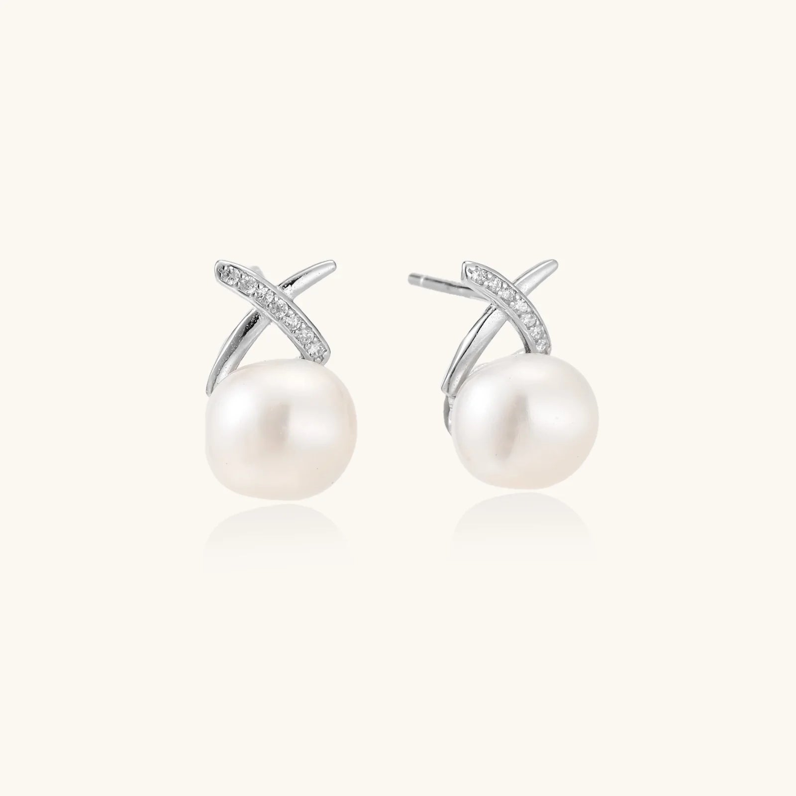 Rhodium-plated silver stud earrings with sparkling X design above lustrous round freshwater pearls on white background.