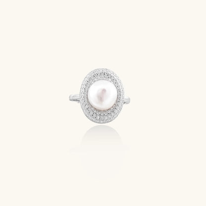 Silver ring with lustrous white pearl center surrounded by sparkling crystal halo on light background.