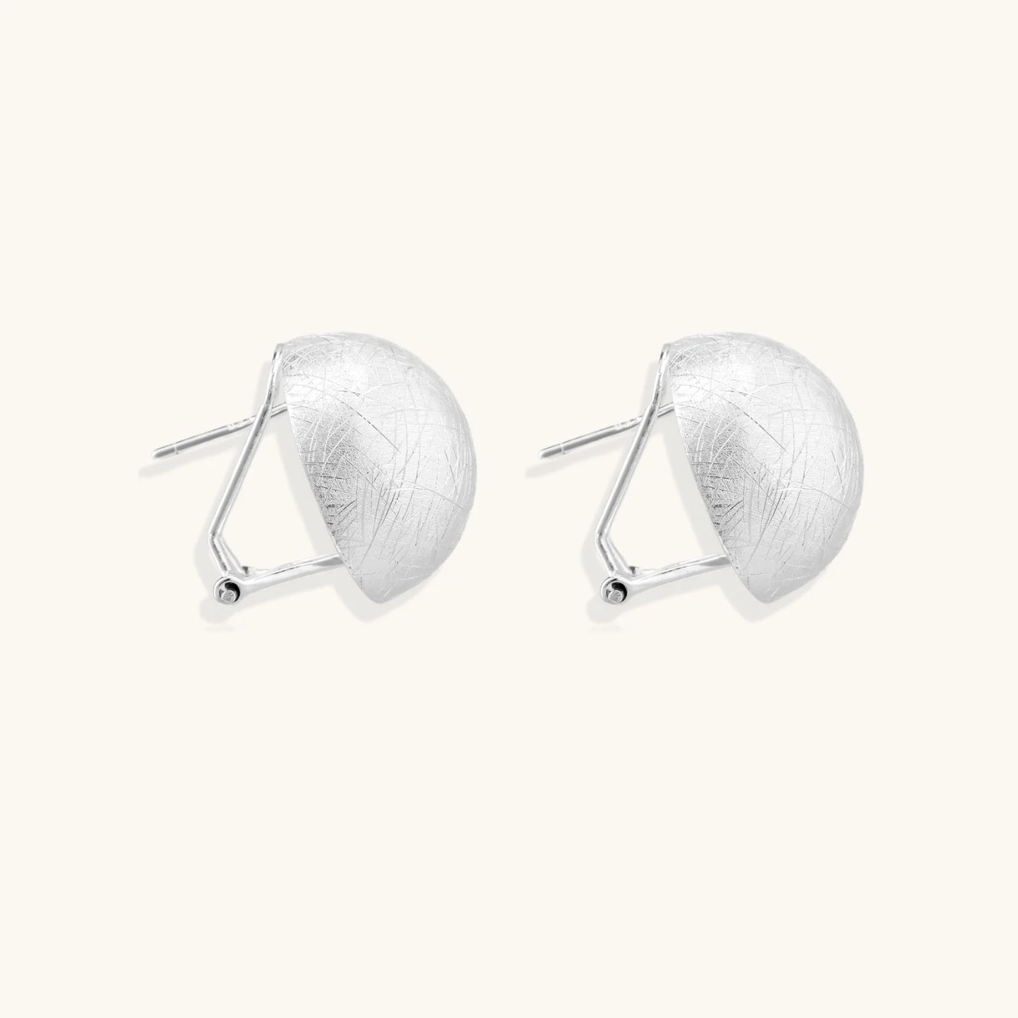 Brushed sterling silver half-dome clip-on earrings with textured surface against cream background