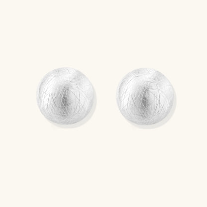 Brushed sterling silver half-dome clip-on earrings with textured surface against cream background