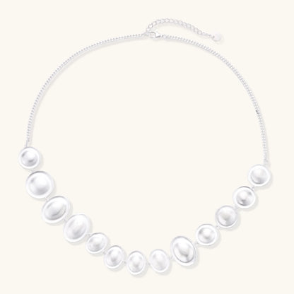 Graduated pearl-finish silver discs forming an organic bubble bib necklace on delicate chain against cream background.