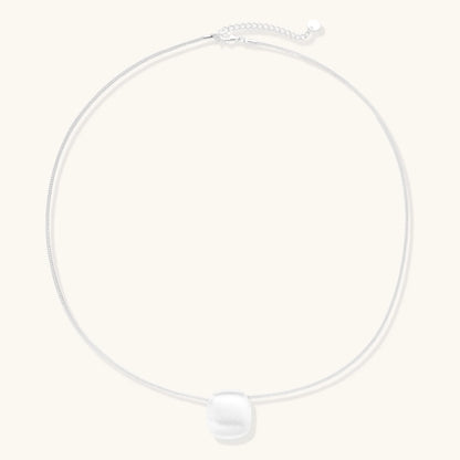 Minimalist brushed sterling silver dome pendant on delicate chain against cream background, showing matte textured finish