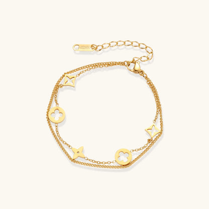 Double-layer gold-plated bracelet with quatrefoil and star charms on cream background, 18K gold finish.