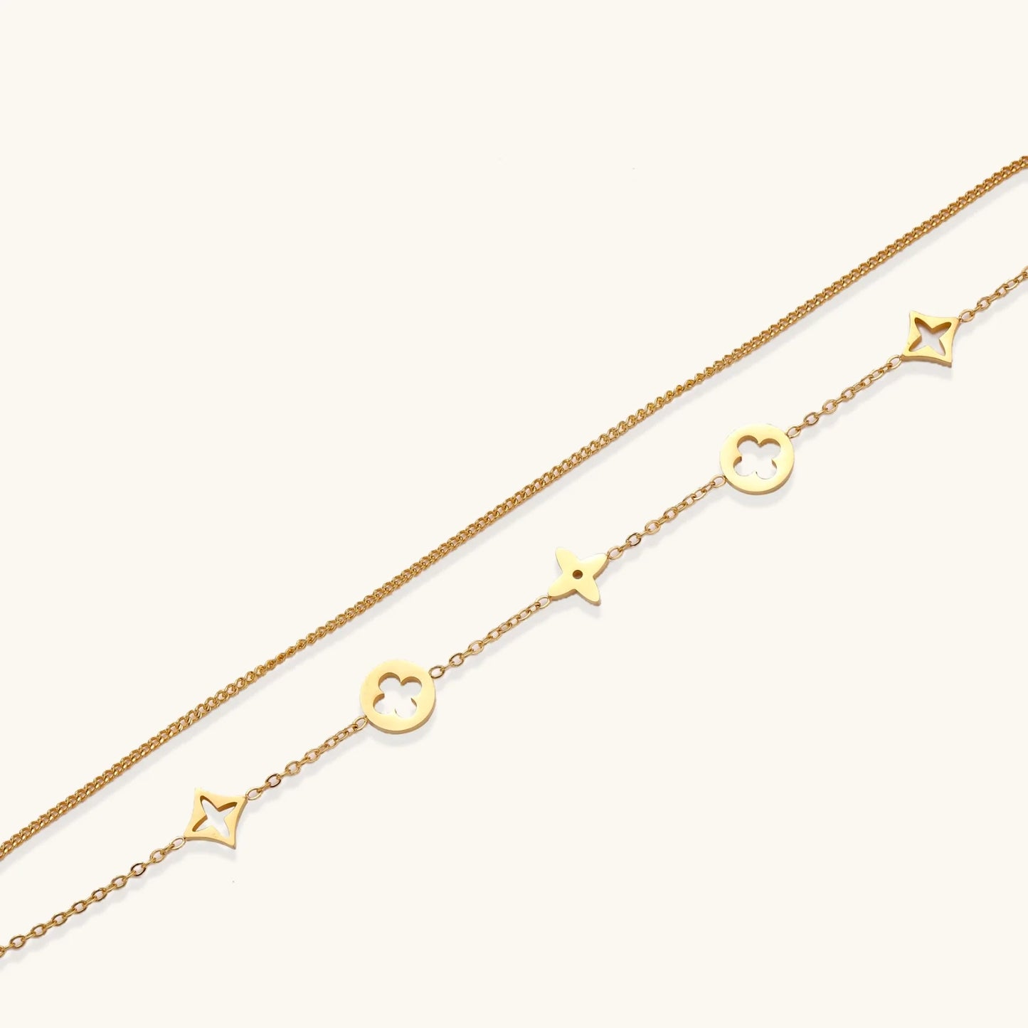 Double-layer gold-plated bracelet with quatrefoil and star charms on cream background, 18K gold finish.