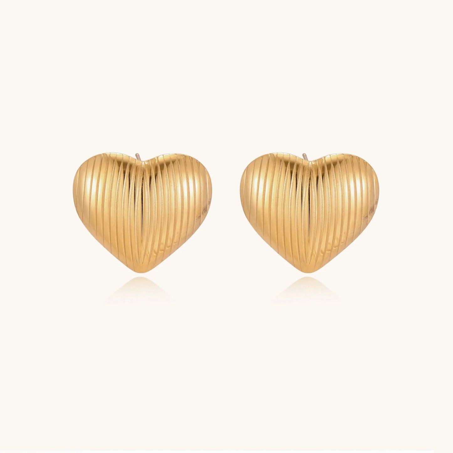 Gold heart-shaped stud earrings with parallel ridged texture on cream background