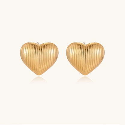 Gold heart-shaped stud earrings with parallel ridged texture on cream background