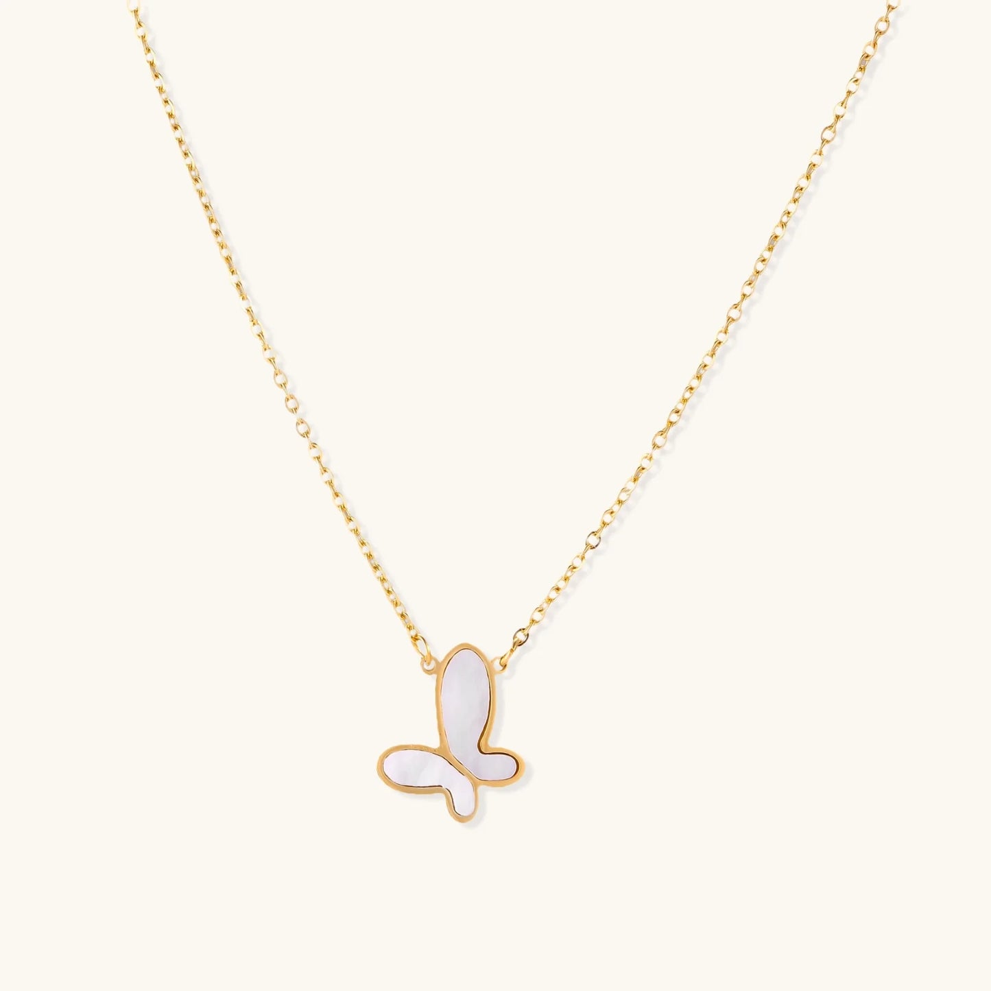 Gold-plated butterfly pendant with iridescent mother of pearl inlay on delicate chain against cream background.