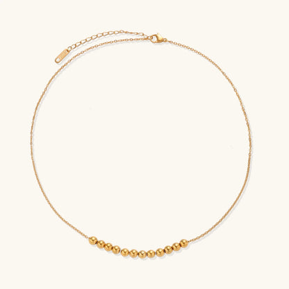Delicate gold-plated necklace with graduated spherical beads forming gentle smile curve on beige background